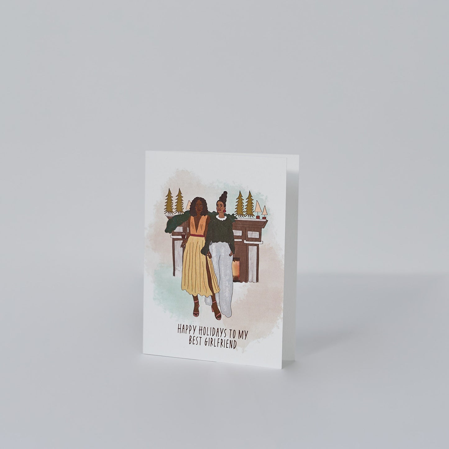 holiday card on white background with illustration of two black women dressed in holiday attire standing in front of fireplace with mini christmas trees