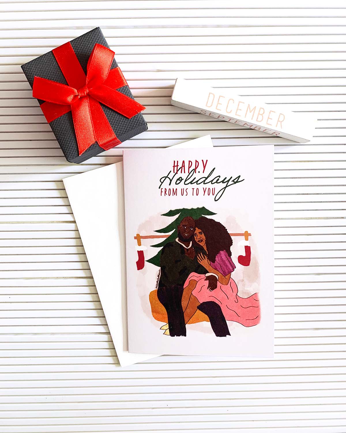 greeting card mock up of black couple sitting together on a yellow cushion with words above them reading happy holidays from us to you