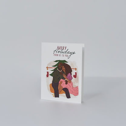 white card that reads happy holidays from us to you with illustration of a black couple sitting together in festive attire