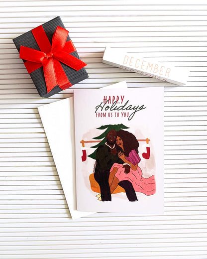 greeting card mock up of black couple sitting together on a yellow cushion with words above them reading happy holidays from us to you